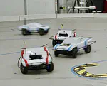 Dynamic Multi-Team Racing: Competitive Driving on 1/10-th Scale Vehicles via Learning in Simulation